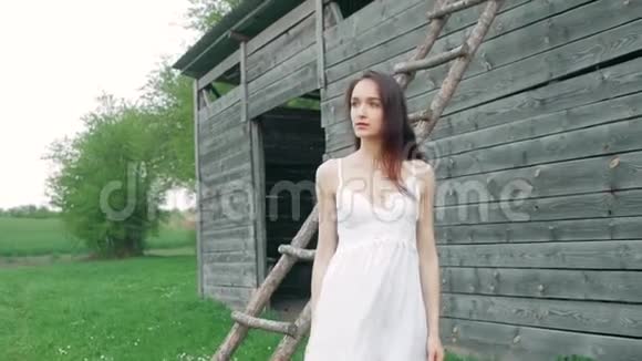 春天的时尚肖像一位美丽快乐的年轻女子穿着白色连衣裙棕色长发靠近木制仓库视频的预览图