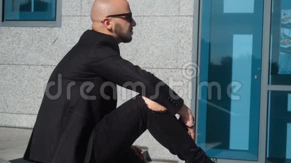 穿着黑色西装戴太阳镜的年轻商人在街上休息视频的预览图