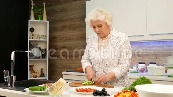 老灰头发的女人在厨房里切黄瓜视频的预览图