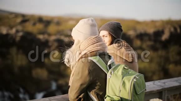 两个旅行的女人站在桥上聊天两个女人在刮风的日子里欣赏风景视频的预览图