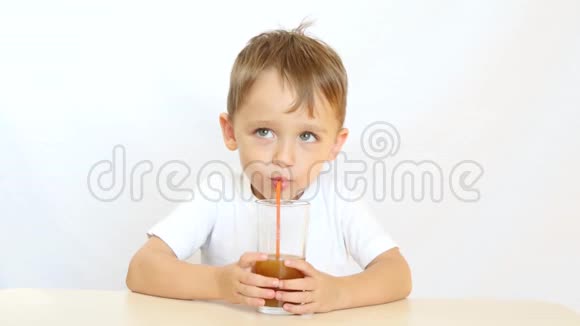 一个快乐的孩子正在用吸管喝果汁坐在桌子旁微笑视频的预览图