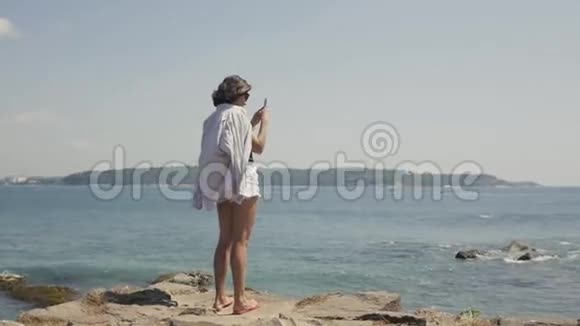 一位年轻女子在海边度假时用手机摄像机拍照的后景视频的预览图
