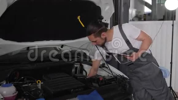 修理年轻的好师傅在汽车车间靠近敞篷专业服务汽车与平板电脑检查发动机视频的预览图