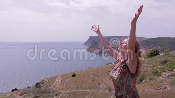 女人站在海边的山上刮风的日子举起手来视频的预览图