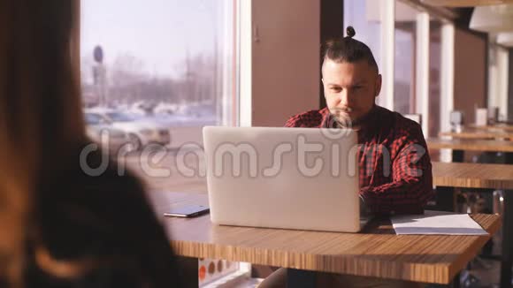 小胡子商人坐在餐桌旁的咖啡馆里在笔记本电脑上人在工作在学习在线教育营销视频的预览图