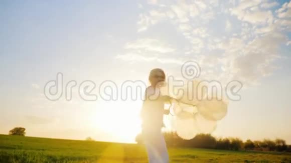 日落时分带着气球在绿色草地上散步的无忧无虑的年轻女人概念轻盈和行动自由视频的预览图