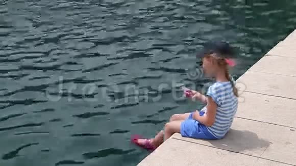 快乐的女孩与旋转者坐在码头附近的海洋悬挂她的腿小女孩在玩她的脚和唱歌视频的预览图