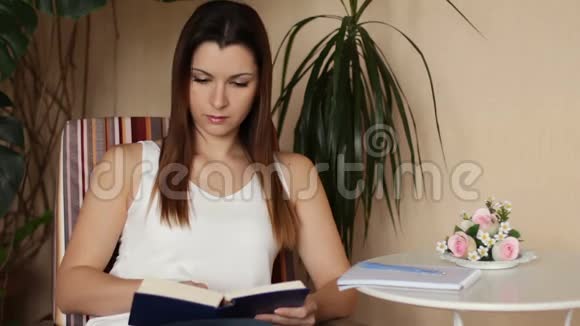 年轻漂亮的女人看书和做笔记坐在椅子上看书的女人视频的预览图