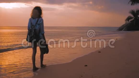 背着背包在海滩上行走的女人在夕阳的灯光下稳稳地拍着视频的预览图