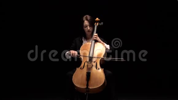 女孩在黑暗的房间里坐在椅子上玩大提琴黑色背景视频的预览图