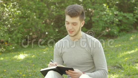 帅哥坐在公园的草地上在书上做笔记视频的预览图