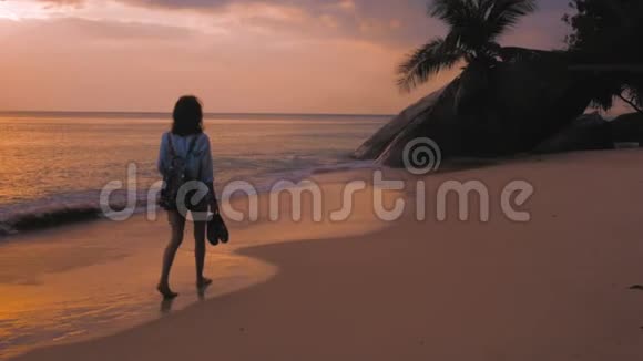 背着背包在海滩上行走的女人在夕阳的灯光下稳稳地拍着视频的预览图