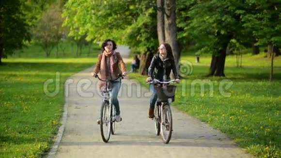 两个活跃的女孩一起在城市公园骑马带着自行车的年轻女人微笑视频的预览图