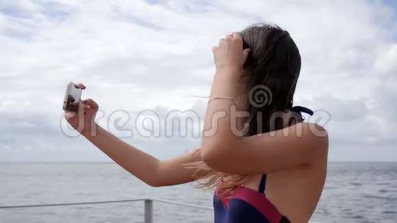 海边穿泳衣戴牙套的自拍女孩智能手机上长发女性的照片背景是视频的预览图