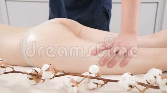 男性理疗师在按摩治疗前在女性大腿和臀部摩擦按摩油的特写视频的预览图