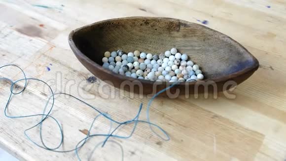 编织珠子在木碗中特写蓝色珠子形状像木桌上的船视频的预览图