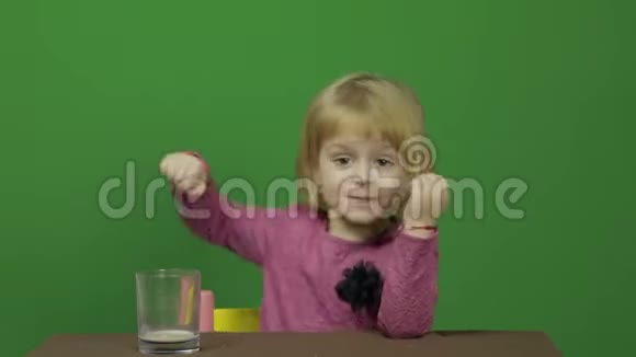 女孩坐在桌子旁喝可可快乐的三岁女孩可爱的女孩微笑可爱的小孩视频的预览图