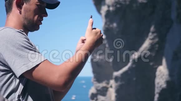 一个好人把岩石和波浪的照片拍进相机双手做手势胜利高清1920x1080慢动作视频的预览图