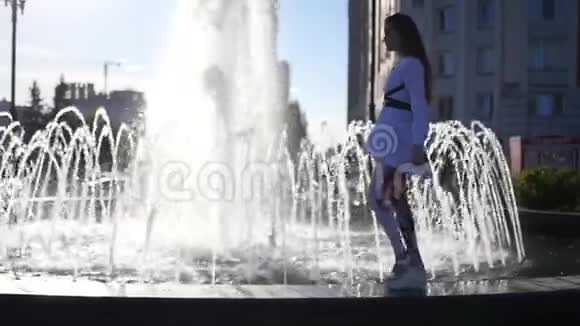 一个美丽的模特女孩走在喷泉的边缘有美丽的亮点高清1920x1080慢动作视频的预览图