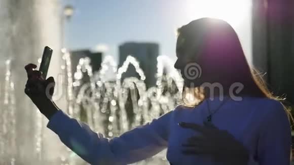一个留着长发的漂亮女孩在镜头前摆姿势用模糊的光线站在喷泉前拍照视频的预览图