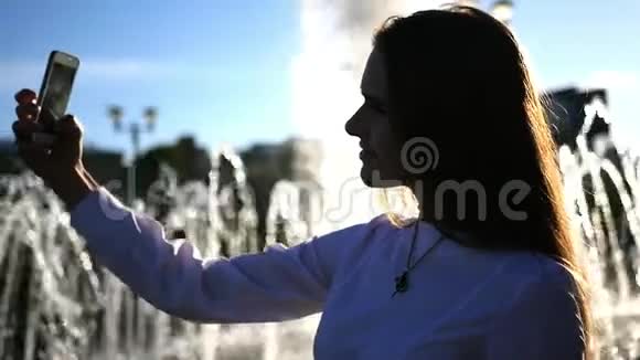 一个留着长发的年轻女孩在镜头前摆姿势在城市的喷泉附近拍照镜头的效果视频的预览图