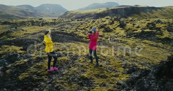 科普特在冰岛熔岩上拍摄的两名女子附近飞行在山上拍照的游客视频的预览图