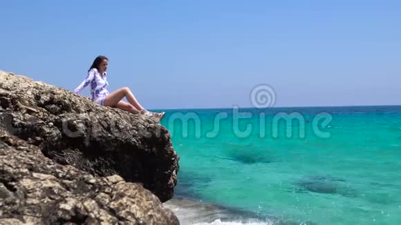 漂亮的女人坐在靠近水的石头上美丽的女人坐在海边的岩石上视频的预览图