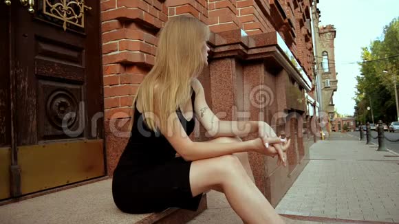 漂亮的金发女郎穿着黑色的裙子坐在街上视频的预览图