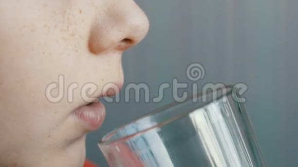一个有蓝眼睛和雀斑的少年从一个有奶胡子的玻璃烧杯里喝牛奶视频的预览图