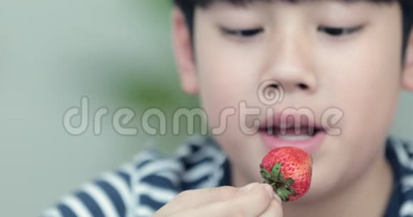 可爱的亚洲男孩带着微笑在家吃草莓视频的预览图