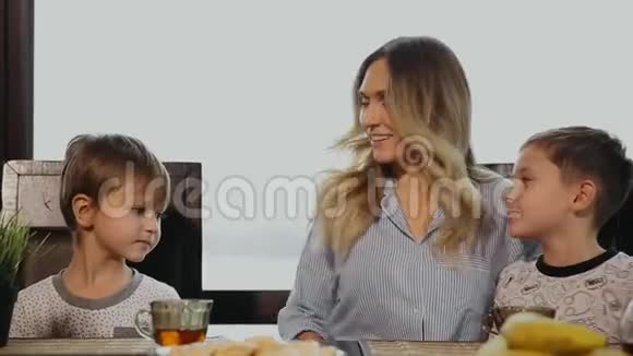妈妈在厨房里拥抱和亲吻他们的孩子吃早餐嘲笑孩子们视频的预览图