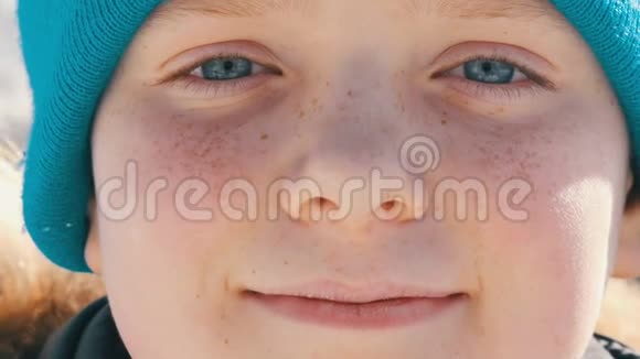 一个年轻的男孩有着一双不寻常的绿松石眼睛脸上有雀斑戴着一顶蓝色帽子看着相机和照片视频的预览图