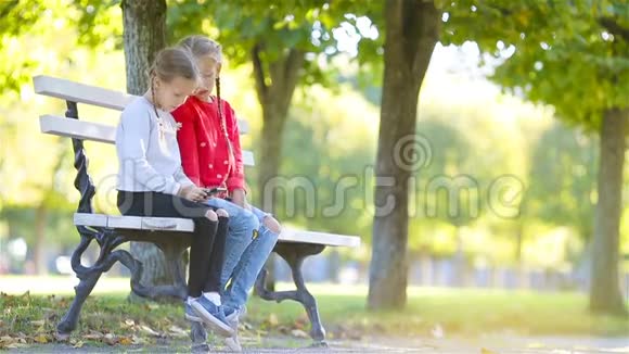 小可爱的女孩带着智能手机在秋天的户外孩子们在秋天公园的温暖的晴天里玩视频的预览图