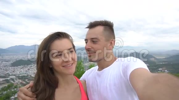 幸福微笑的情侣录制视频在山上自拍具有空中城市视野男人亲吻女孩视频的预览图