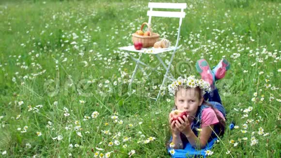 在一片洋甘菊的草坪中间一个七岁的漂亮姑娘躺在草地上戴着雏菊花圈兴高采烈视频的预览图