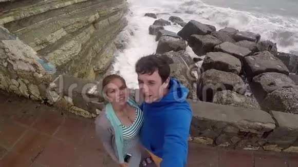 一对年轻夫妇一男一女站在码头上在海滩上自拍海浪拍打着大石头慢慢慢慢视频的预览图