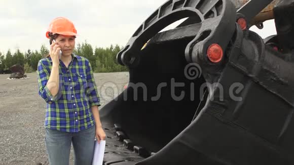 女工程师站在挖掘机的一个钢包旁边检查一个方案视频的预览图