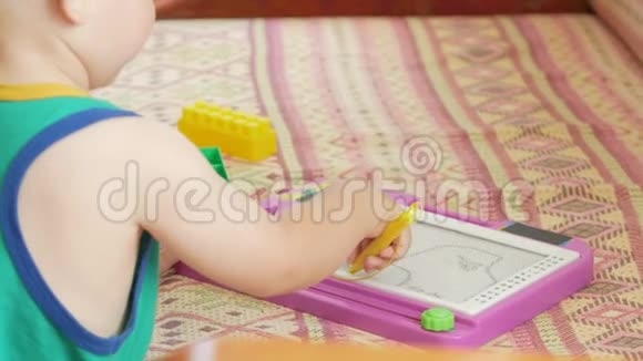 一个2岁的好男孩在一个磁性画板上画画他有许多难以理解的人物孩子很努力视频的预览图