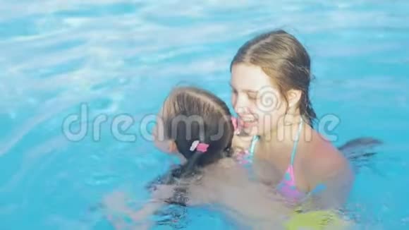 美丽的女孩教她妹妹在游泳池里游泳视频的预览图
