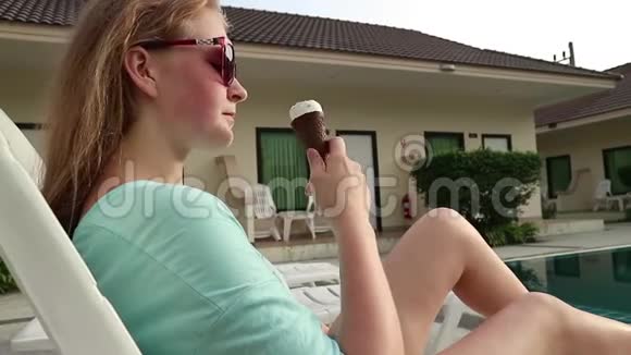 漂亮的金发美女穿着泳衣和太阳镜在酒店游泳池附近吃冰淇淋视频的预览图