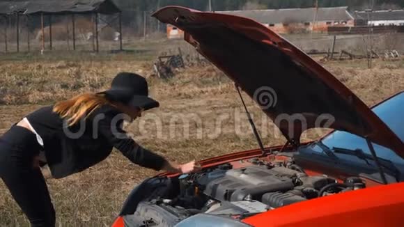 优雅的女孩看着一辆破车的引擎盖下视频的预览图