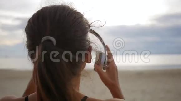 年轻女子戴着耳机在海滩上欣赏音乐从后面看泰国高清慢镜头视频的预览图