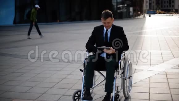 残疾人商人坐在轮椅户外与平板电脑合作视频的预览图