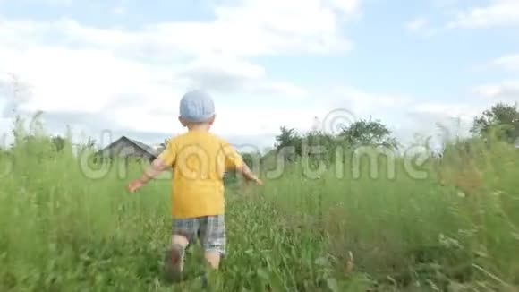 一个可爱的孩子沿着城外的高草奔跑两年来一件黄色的球衣和一顶浅色的帽子视频的预览图