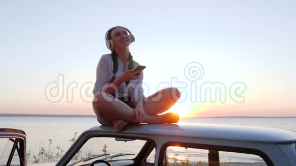 带着蓝牙耳机的女孩在背景夕阳下的路堤上听歌享受夏天的休息背光视频的预览图