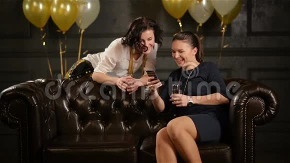 手里拿着香槟酒杯微笑的女人在庆祝时使用智能手机头发短的女士视频的预览图