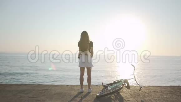 年轻漂亮的长发女人在日落或日出时在海上玩得很开心有自行车的女性视频的预览图