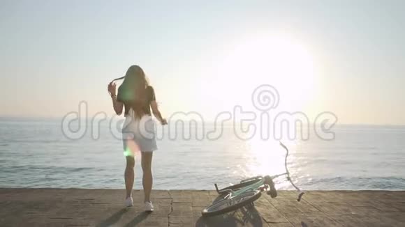 年轻漂亮的长发女人在日落或日出时在海上玩得很开心有自行车的女性视频的预览图