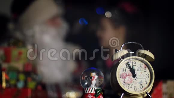 黄昏时分前景是一个闹钟背景是圣诞老人拥抱一个可爱的小女孩视频的预览图