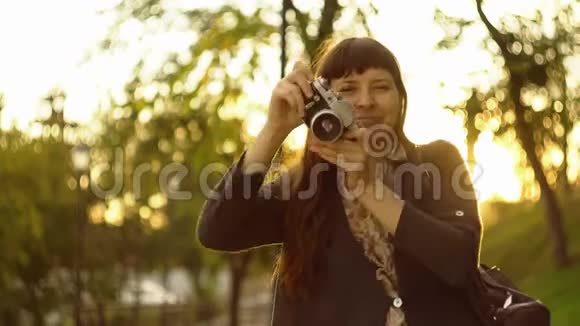 一个年轻的女人在夕阳的光线下在一台旧相机上拍照视频的预览图